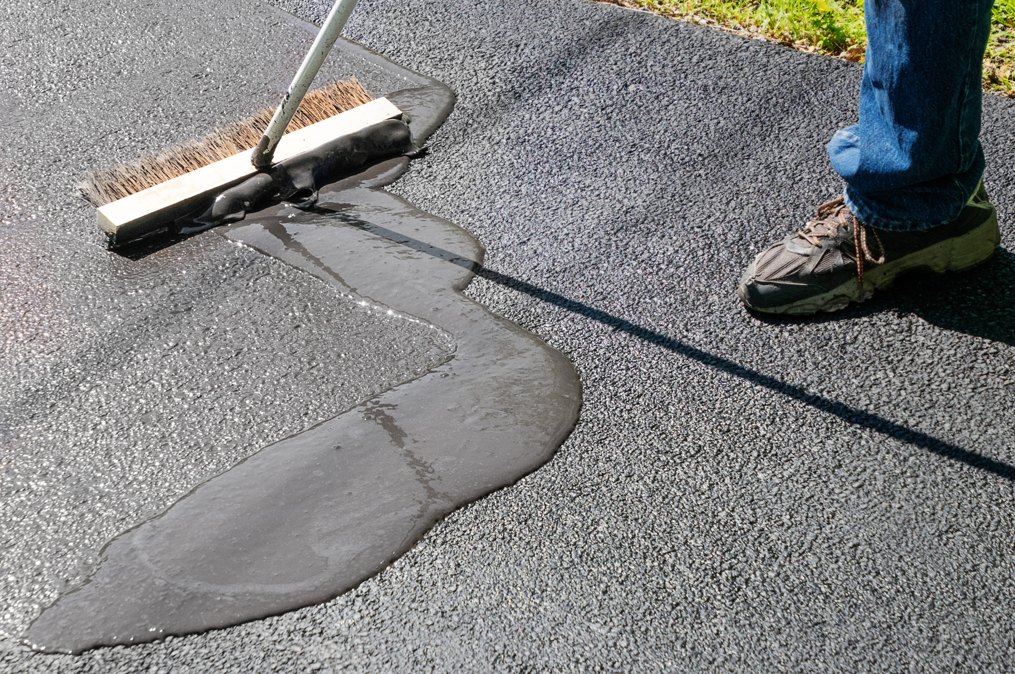 Spreading asphalt resealer onto driveway for maintenance How-Much-Does-It-Cost-to-Build-a-Parking-Lot-Price-Breakdown-for-Asphalt-and-Concrete
